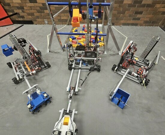 Three robots complete with wheels and crane mechanisms sit on a classroom floor.