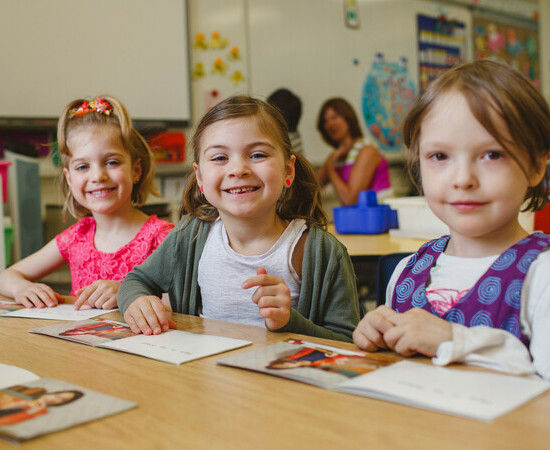 A group of young students sit at a desk together and smile at the camera.