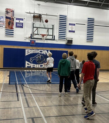 Junior high students take shots at a basketball hoop in a school gym.