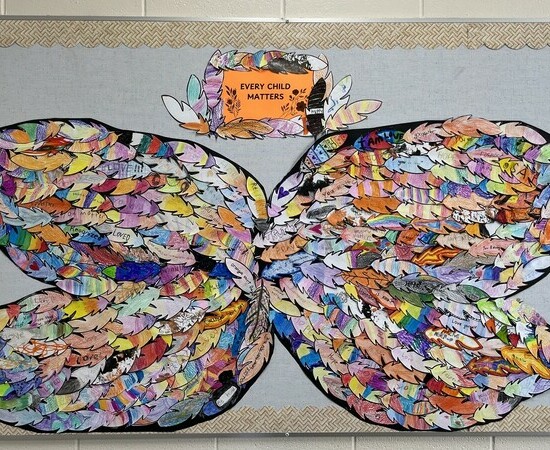 Colorful butterfly wings made of paper feathers are arranged on a bulletin board with a sign reading "Every Child Matters" above.