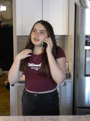 A student stands in a kitchen, where they talk on a wireless handheld phone.