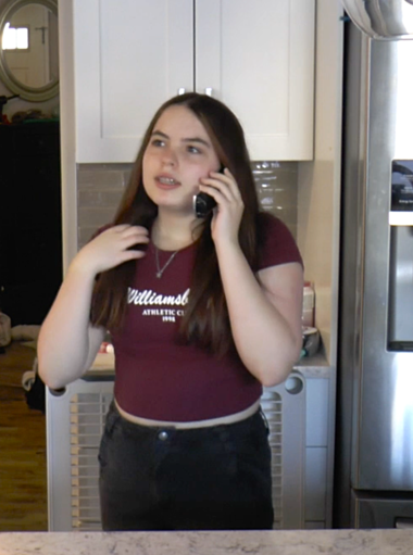 A student stands in a kitchen, where they talk on a wireless handheld phone.