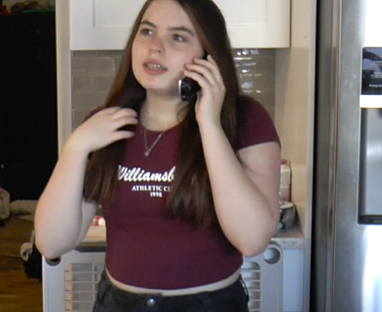 A student stands in a kitchen, where they talk on a wireless handheld phone.