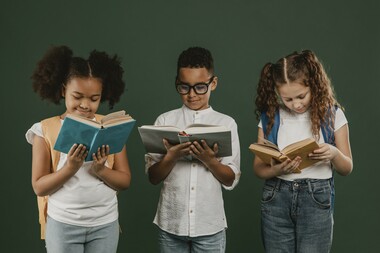 Three students stand in a line, each looking down at a book they have open in their hands.