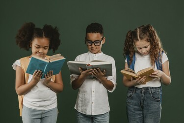 Three students stand in a line, each looking down at a book they have open in their hands.