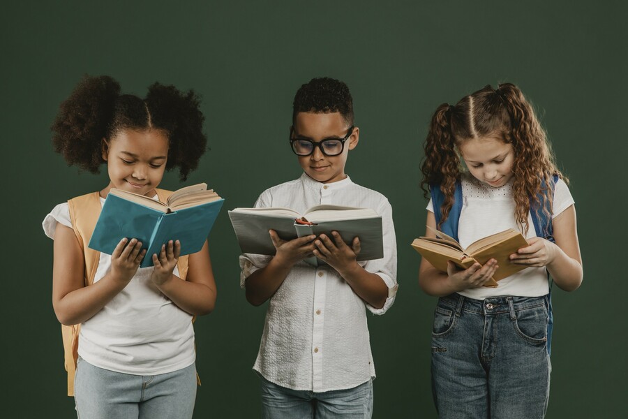 Three students stand in a line, each looking down at a book they have open in their hands.