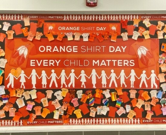 Bulletin board of coloured orange shirt pictures around a sign that reads: Orange Shirt Day Every Child Matters