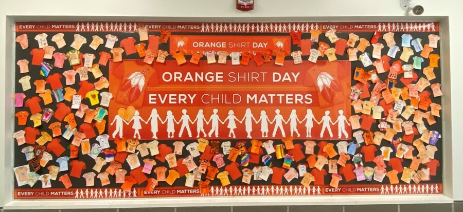 Bulletin board of coloured orange shirt pictures around a sign that reads: Orange Shirt Day Every Child Matters