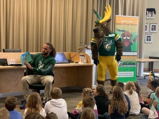Grades 1 and 3 students from Glen Allan Elementary listen to Aaron Grymes read from the Edmonton Elks’ new book.
