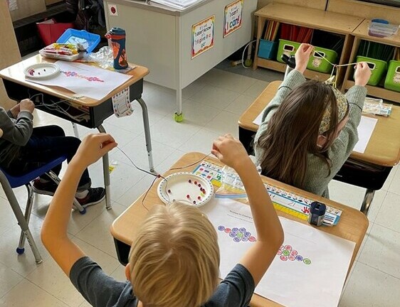 Students sitting at desk stringing beads