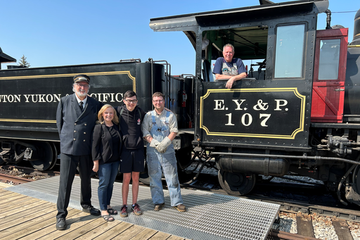 Asher Fehr, a Grade 9 student at Strathcona Christian Academy Secondary, stands next to educational assistant Diane Richards and several park staff near Steam Train 107 at Fort Edmonton Park.