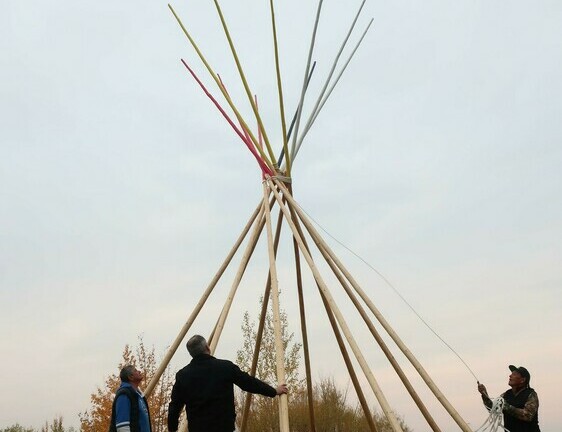 Three men setting up tipi poles outside