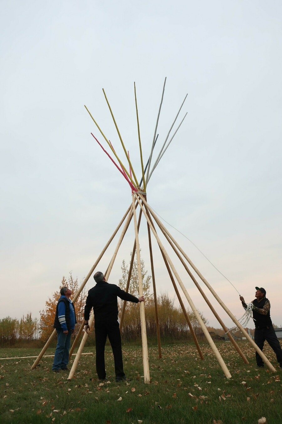 Three adult men setting up tipi poles outdoors